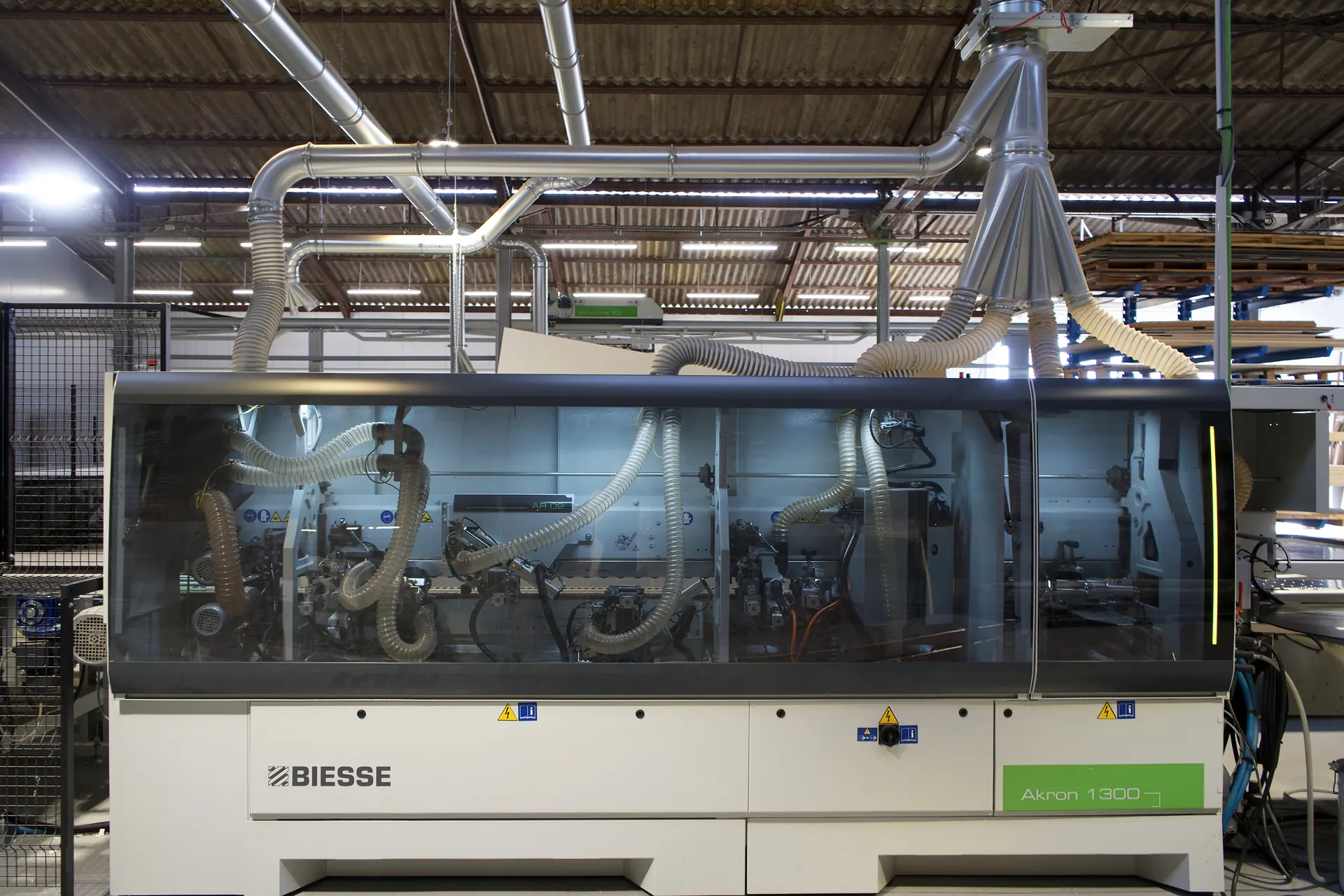 Plaqueuse de chants industrielle vue de face, capot vitré fermé et gaines d'aspiration au-dessus