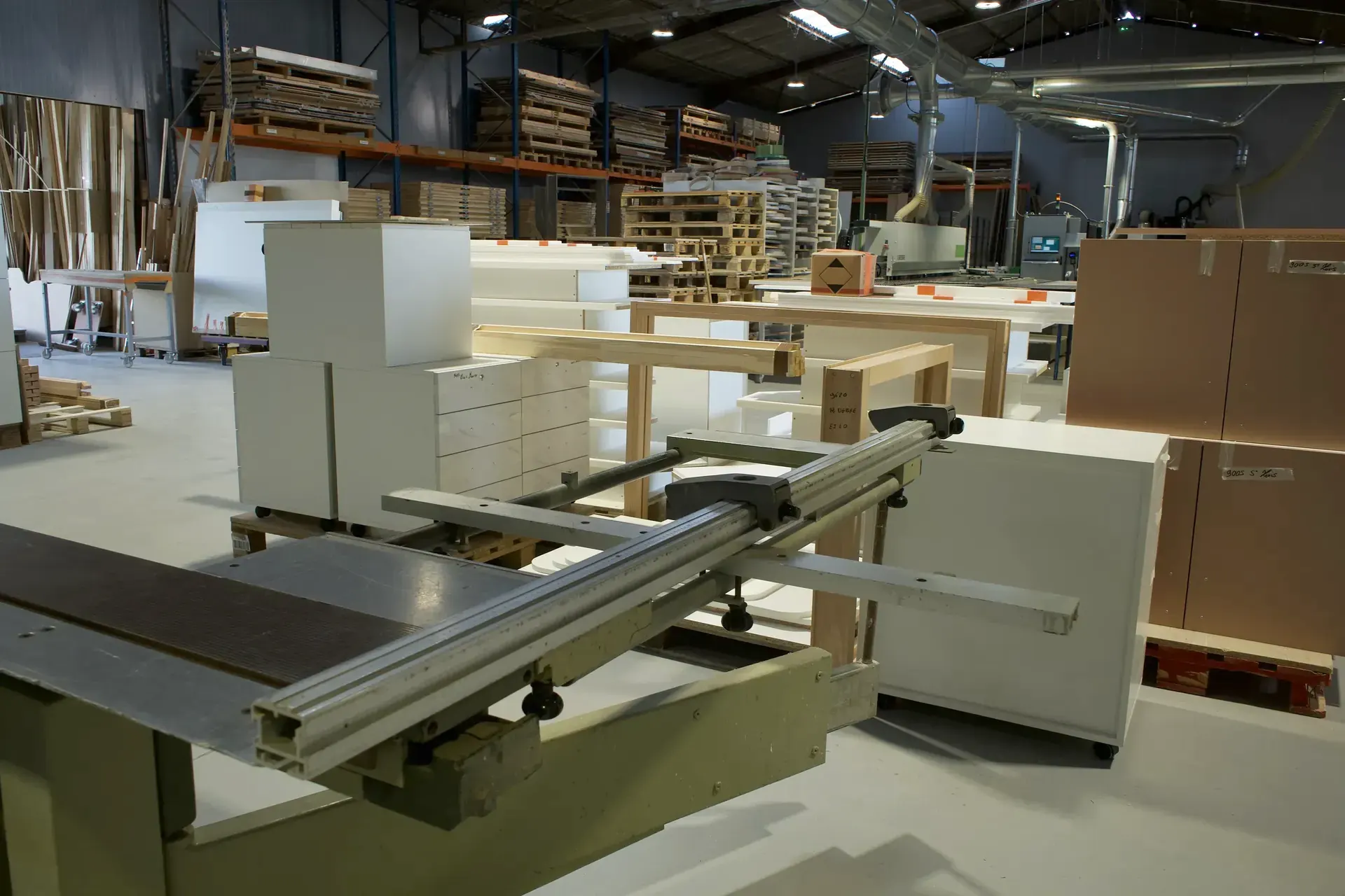 Caissons de meubles blancs à tiroirs assemblés dans l'atelier, derrière le chariot d'une scie à format